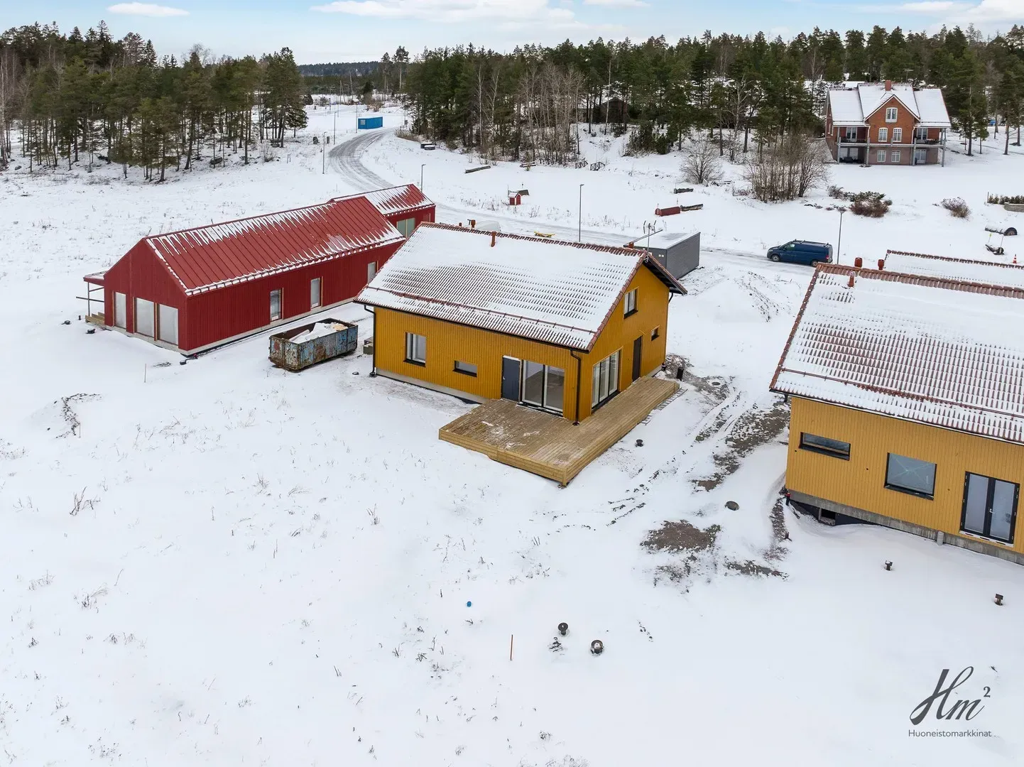 Luminen ilmakuva punaisista ja keltaisista rakennuksista, navetasta ja taloista talvimaisemassa