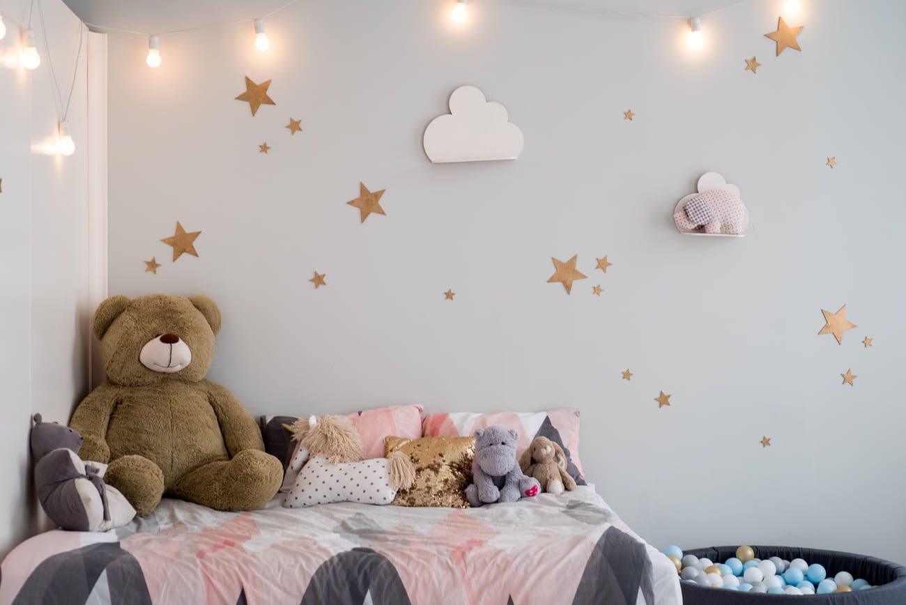 Habitación infantil con cama, osito de peluche, almohadas, calcomanías de estrellas, luces de cadena y piscina de pelotas.