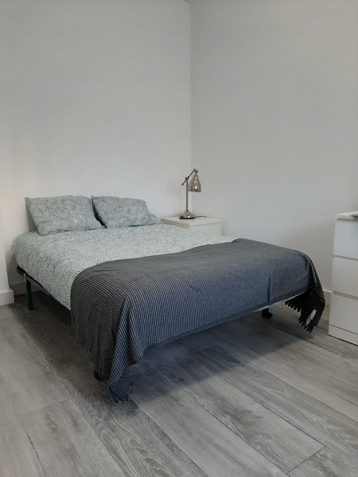 Dormitorio con cama, mesita de noche, lámpara y tocador; combinación de colores gris y blanco.