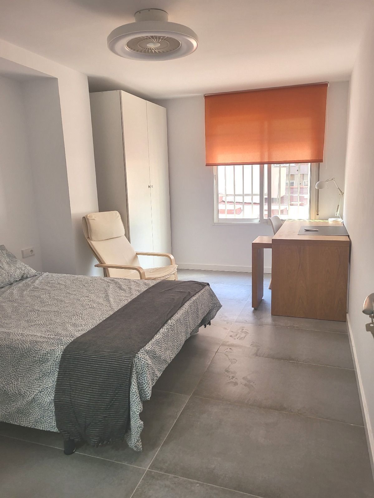 Dormitorio con cama, silla, escritorio, ventana con persiana naranja y armario.