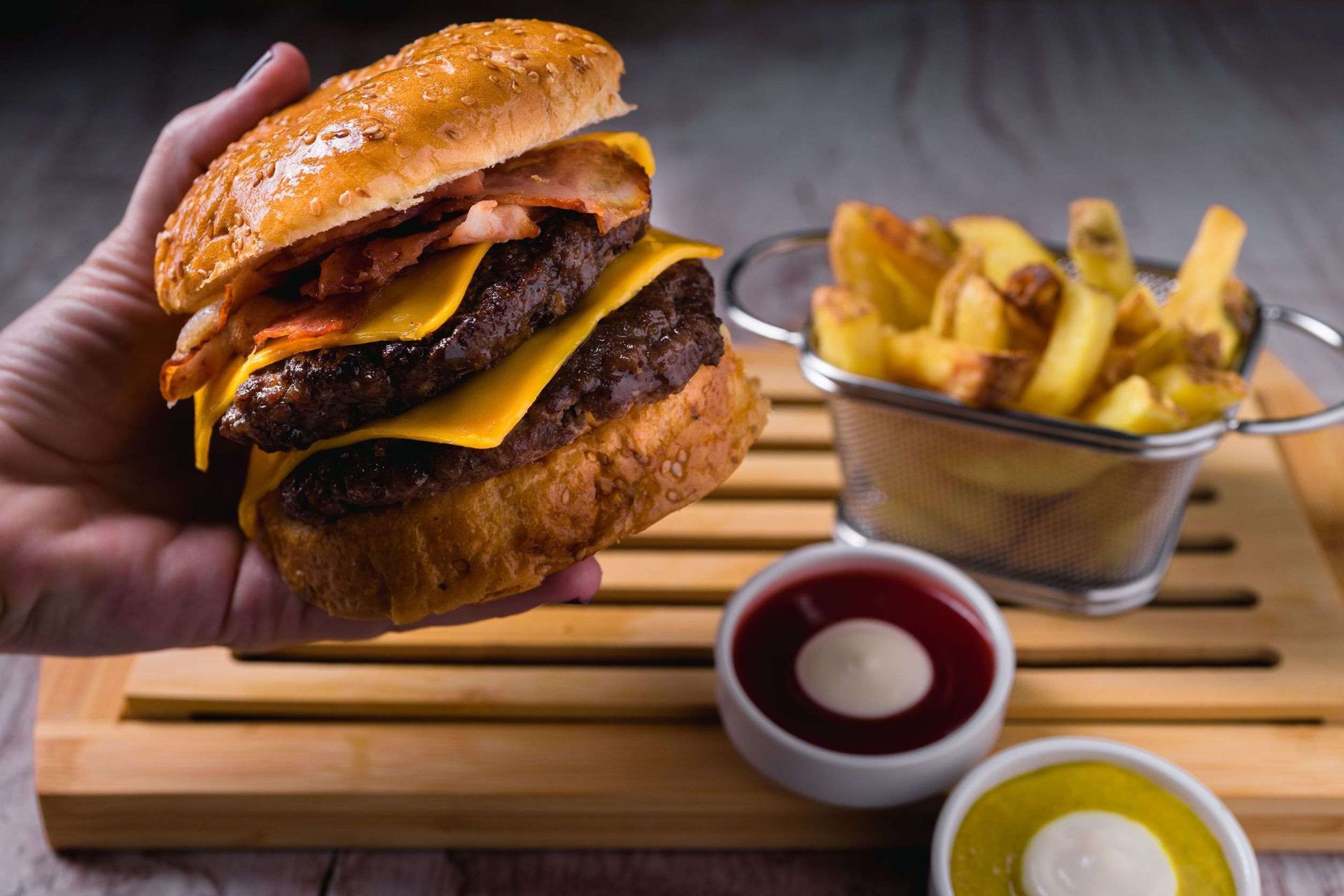 Una persona sostiene una hamburguesa en la mano junto a una canasta de papas fritas.