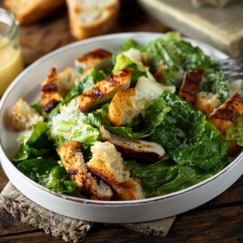Un primer plano de una ensalada César en un recipiente blanco sobre una mesa.