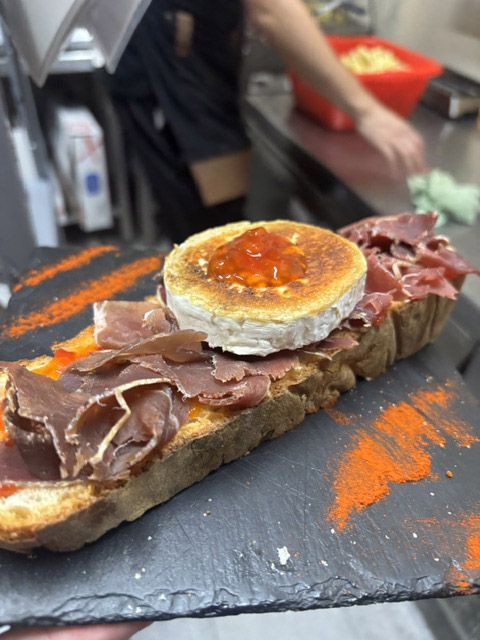 Sándwich abierto con carne en lonchas y huevo escalfado sobre una tabla de pizarra con migas de naranja como guarnición.