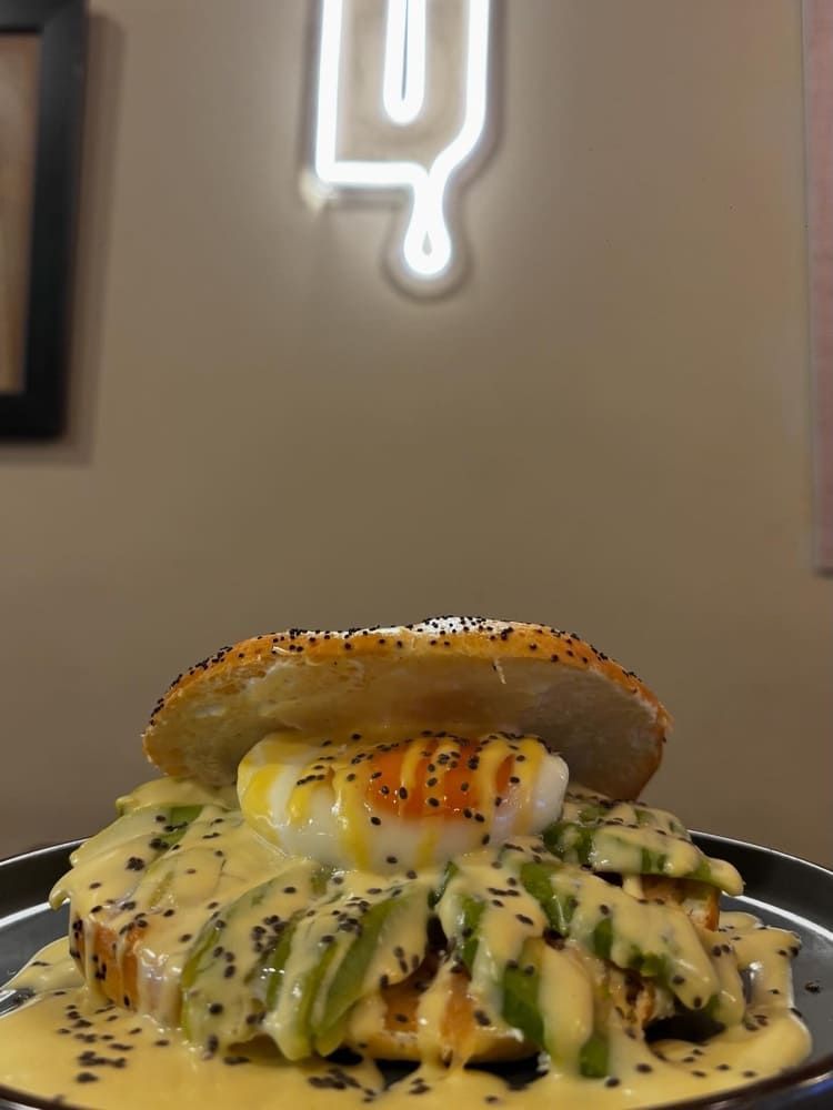Plato salado apilado con aguacate, salsa y un panecillo glaseado en un plato en un ambiente de restaurante con iluminación tenue.