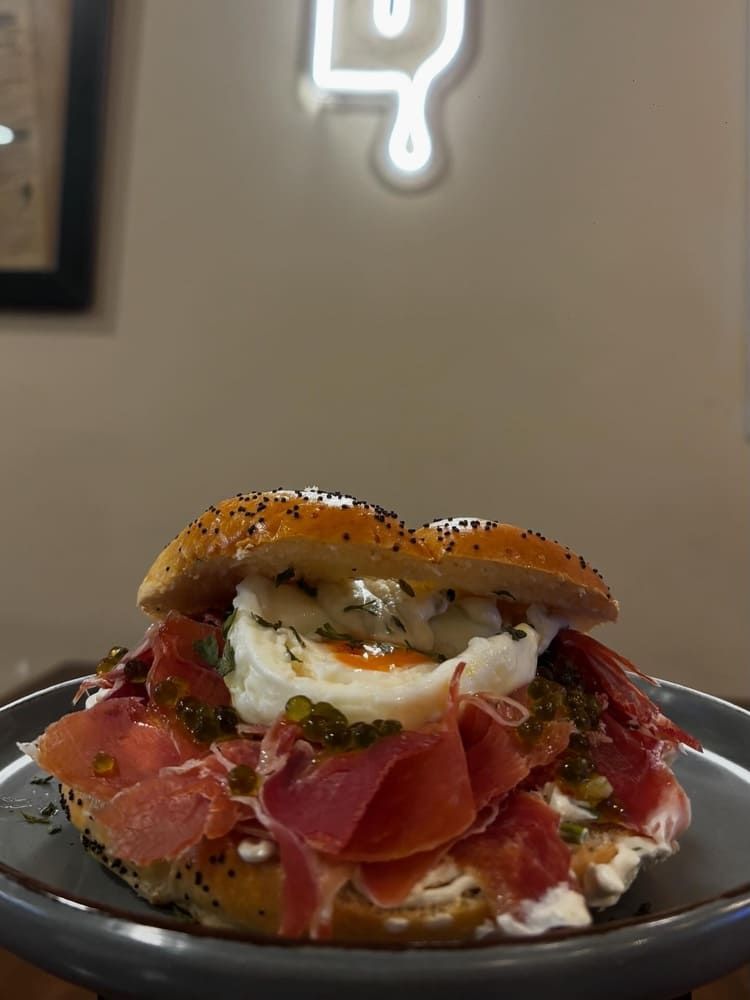 Sándwich de delicatessen con embutidos, huevo escalfado y hierbas aromáticas en un plato negro.