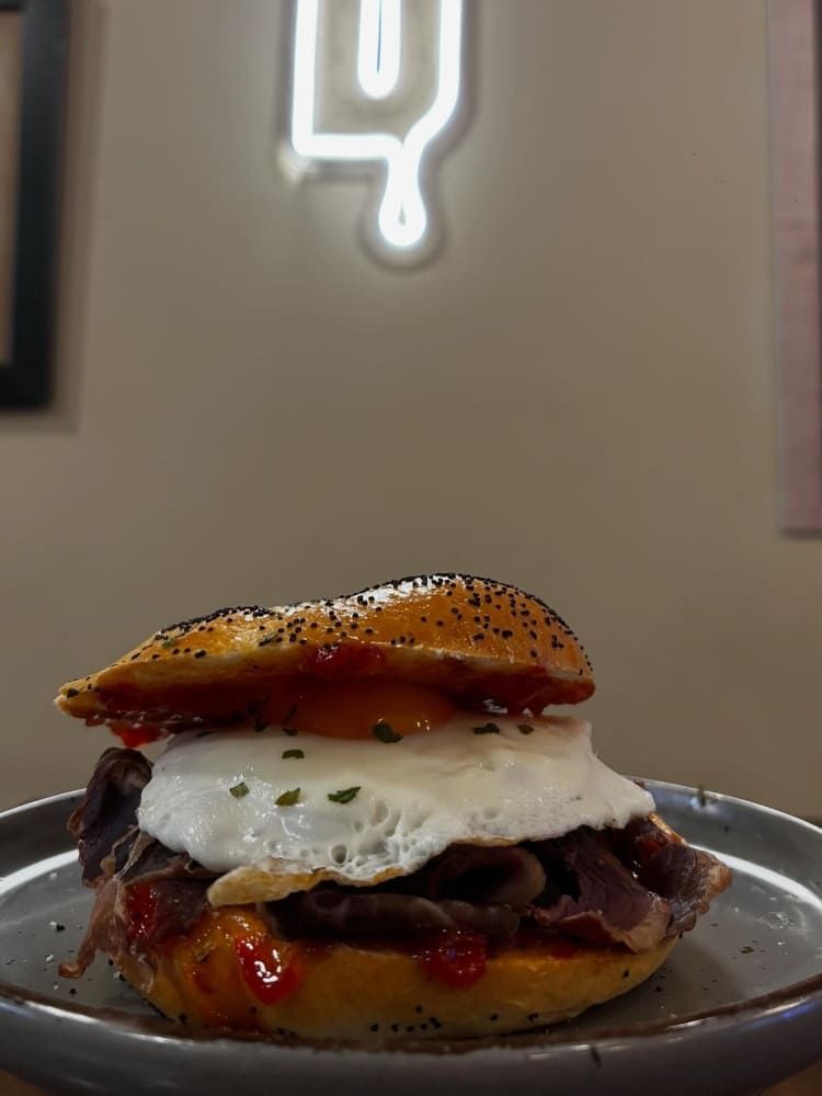 Hamburguesa gourmet con queso fundido y salsa en un plato, con un letrero de neón brillante al fondo.