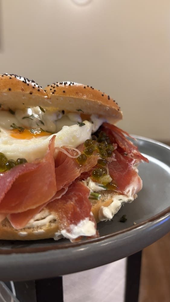 Sándwich de bagel con semillas, prosciutto, queso crema y huevo en un plato.