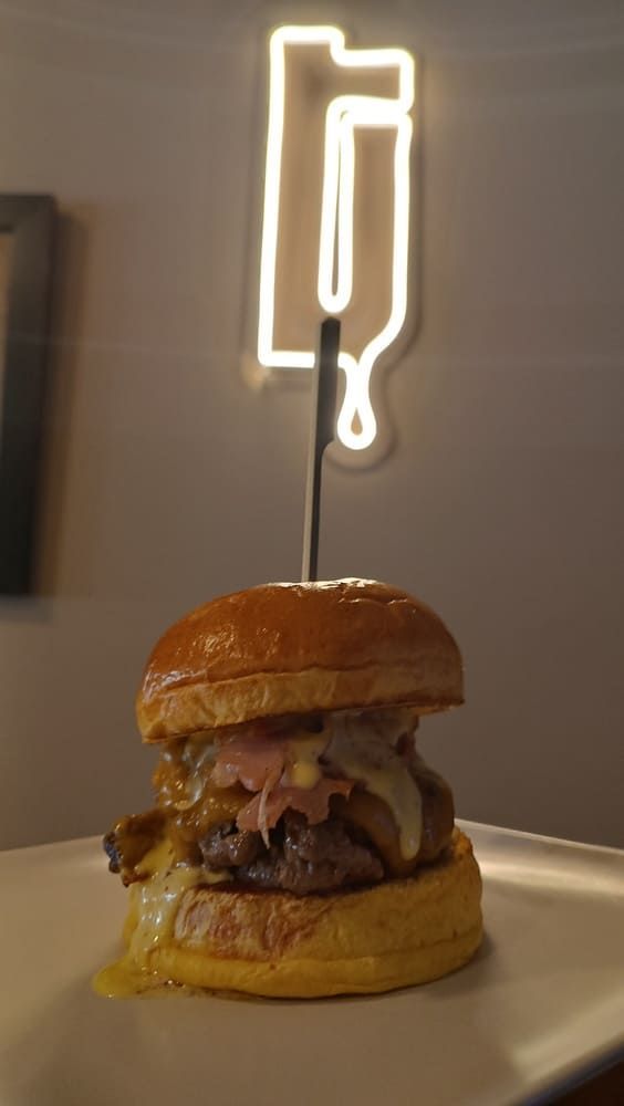 Hamburguesa bajo un letrero luminoso de neón con forma de papas fritas en un plato blanco.