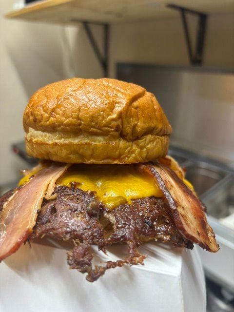 Primer plano de una hamburguesa con queso y tocino en una bandeja en un entorno de cocina.