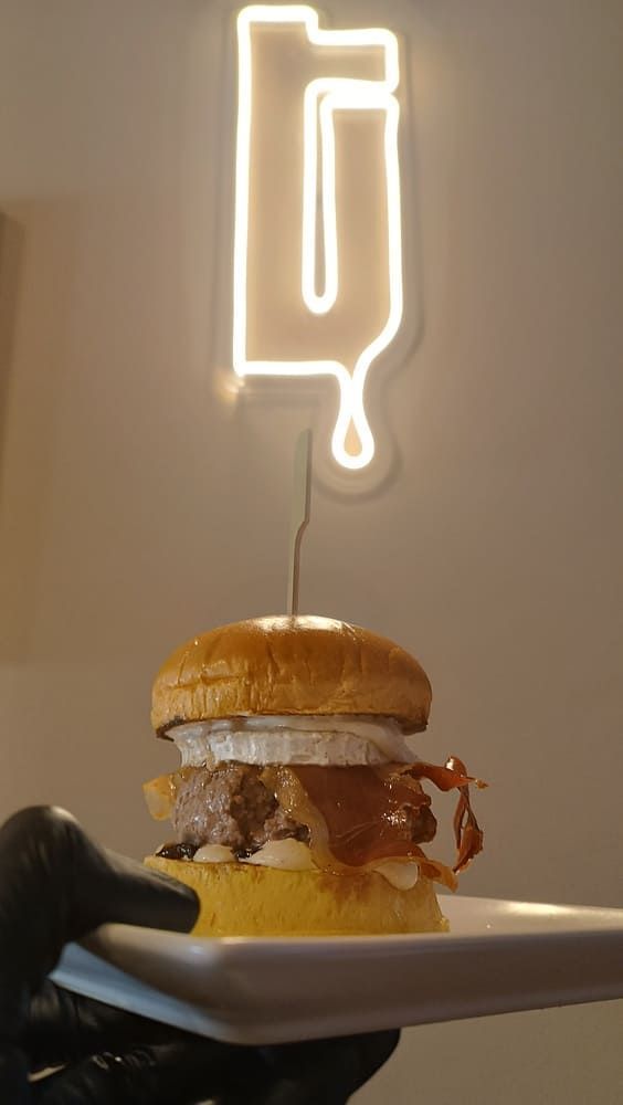 Una hamburguesa en un plato bajo un letrero luminoso de neón con forma de paleta de helado contra una pared lisa.