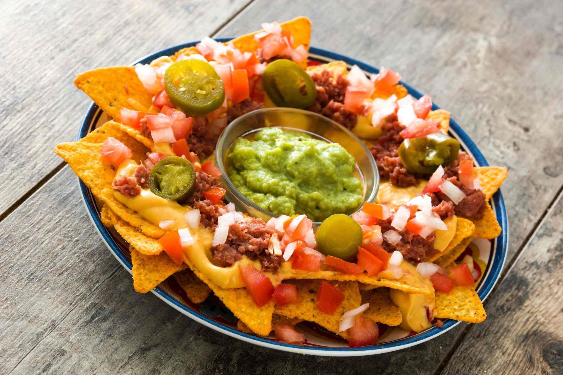 Un plato de nachos con guacamole y salsa en una mesa de madera.