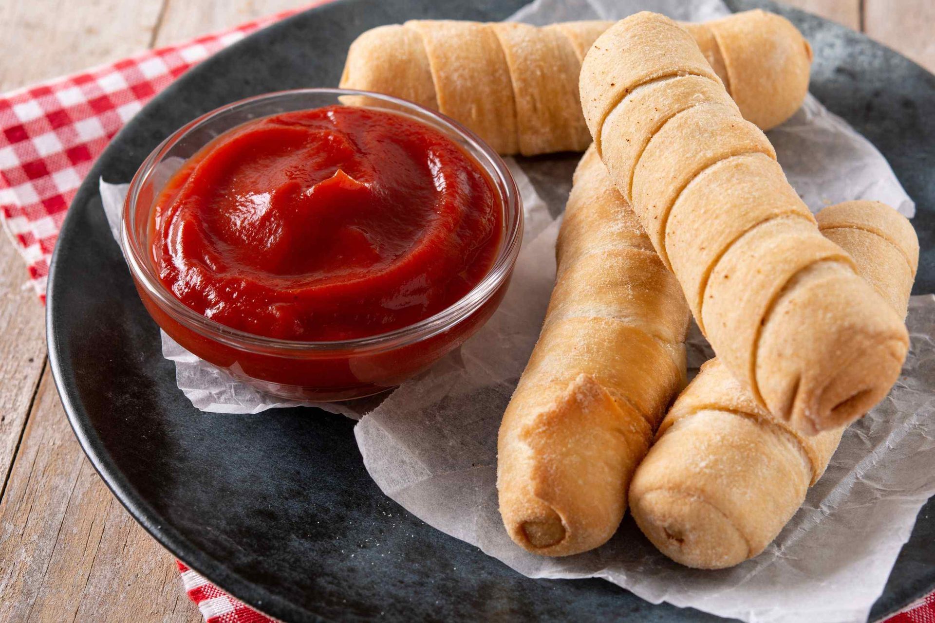 Hay un recipiente con ketchup al lado de un plato de comida.