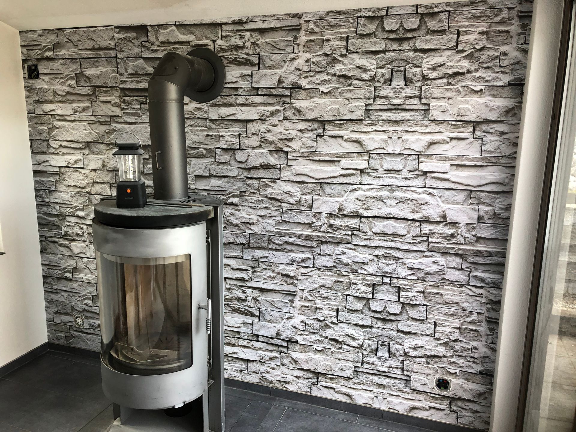 Kamin an einer Steinwand, mit schwarzem Schornstein und kleiner Laterne, in einem Raum.