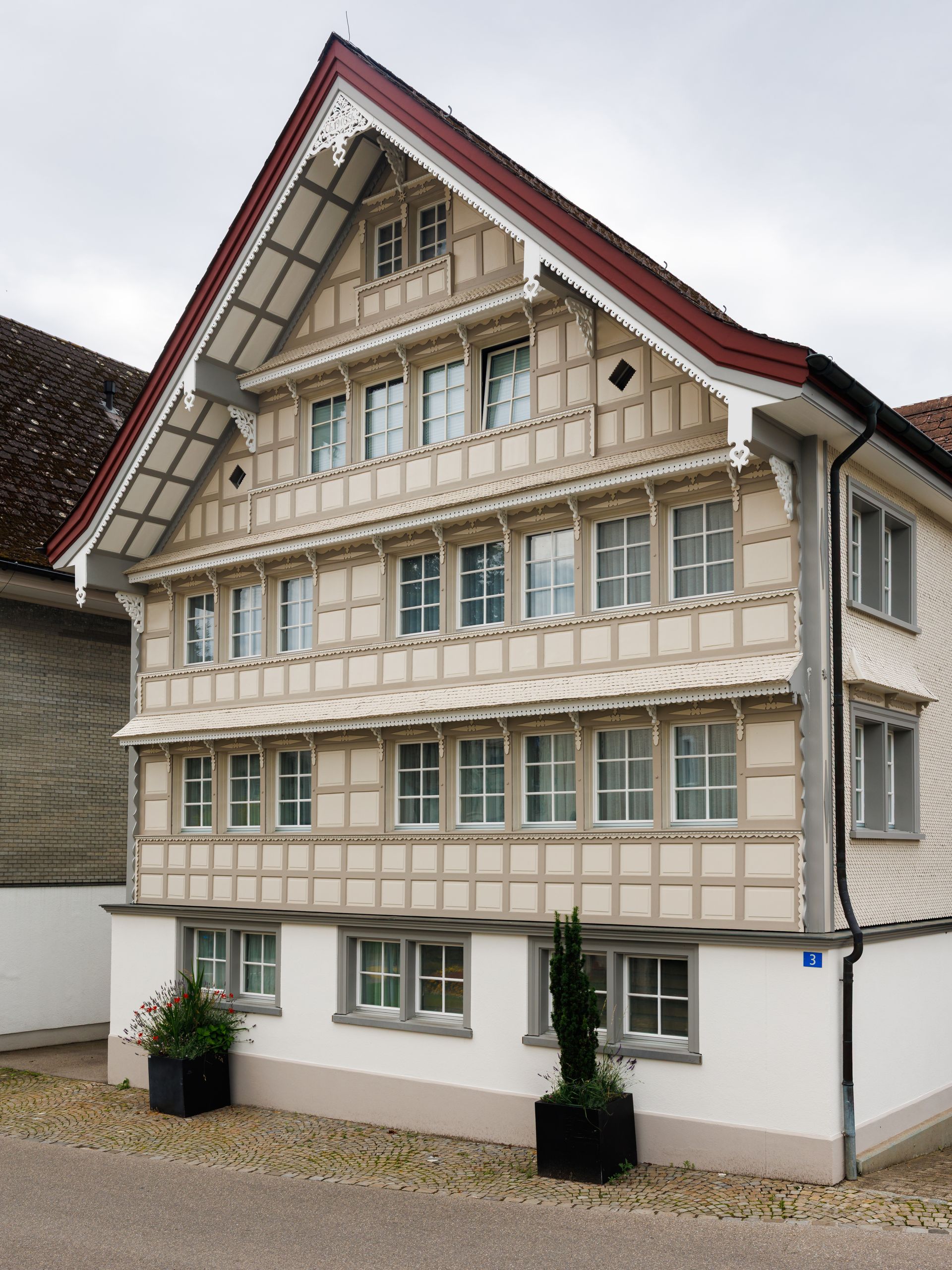 Fachwerkhaus mit Fensterreihen, rotem Dach und weißen Zierleisten in der Schweiz.