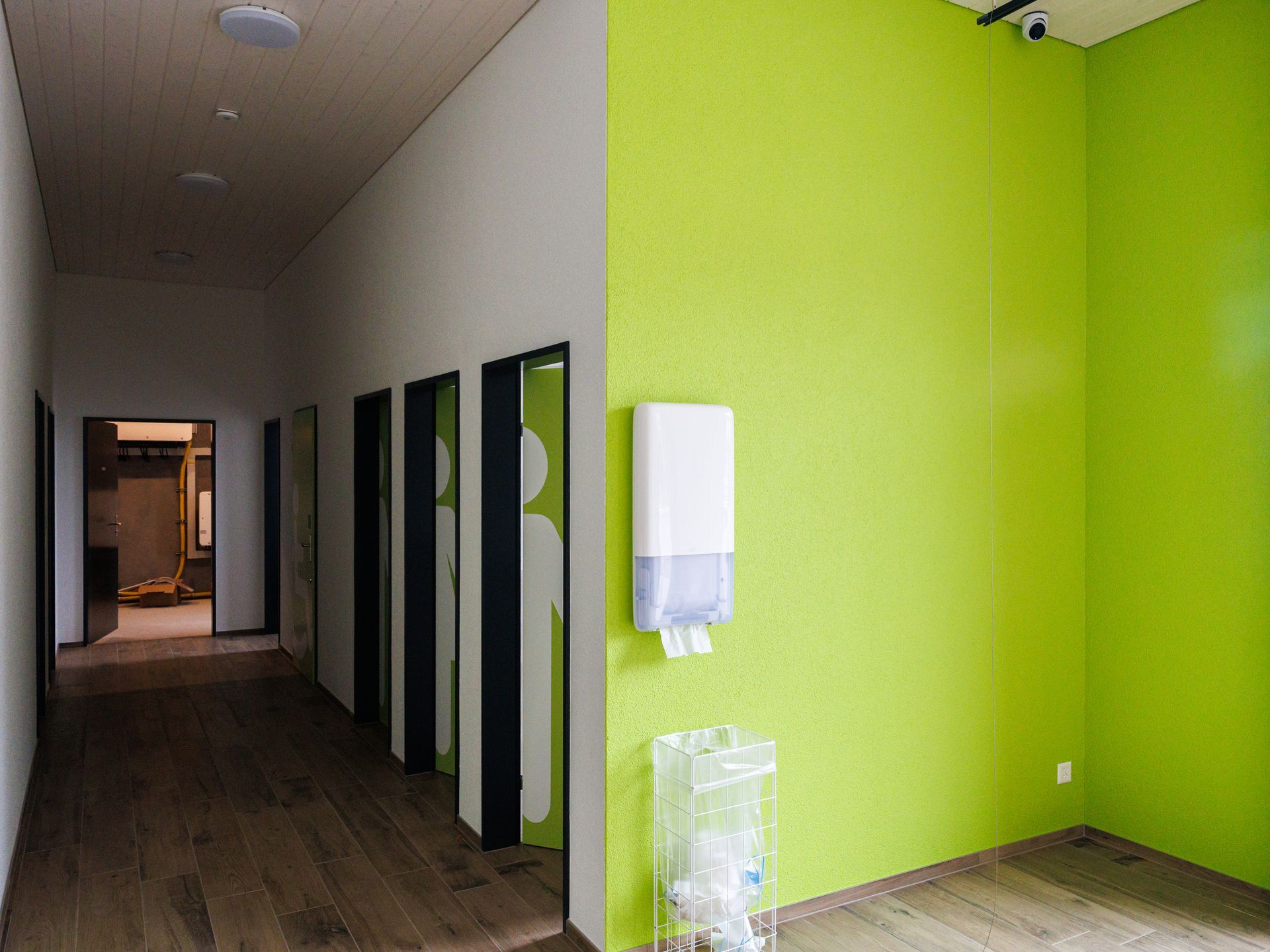Flur mit Holzboden, lindgrüner Wand, weißem Papierhandtuchspender und Kabinen mit grünen Akzenten.