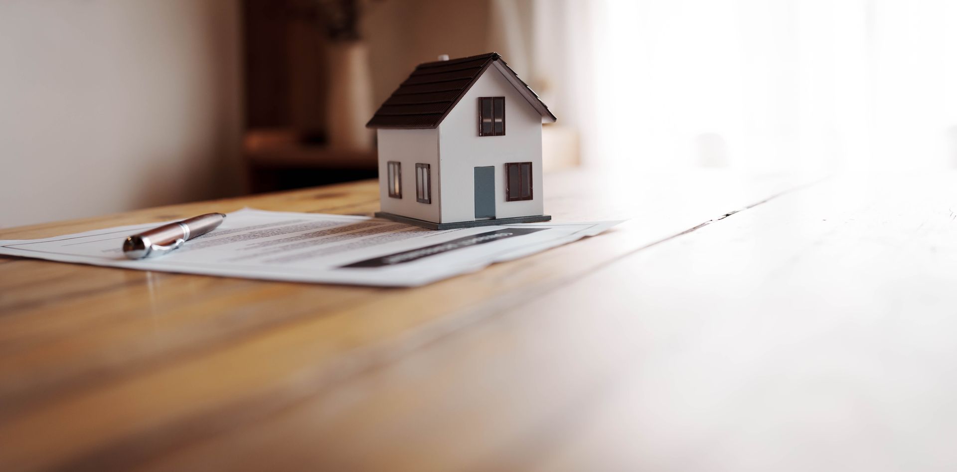 Maquette de maison miniature dessinée au stylo sur un document, posée sur une table en bois.