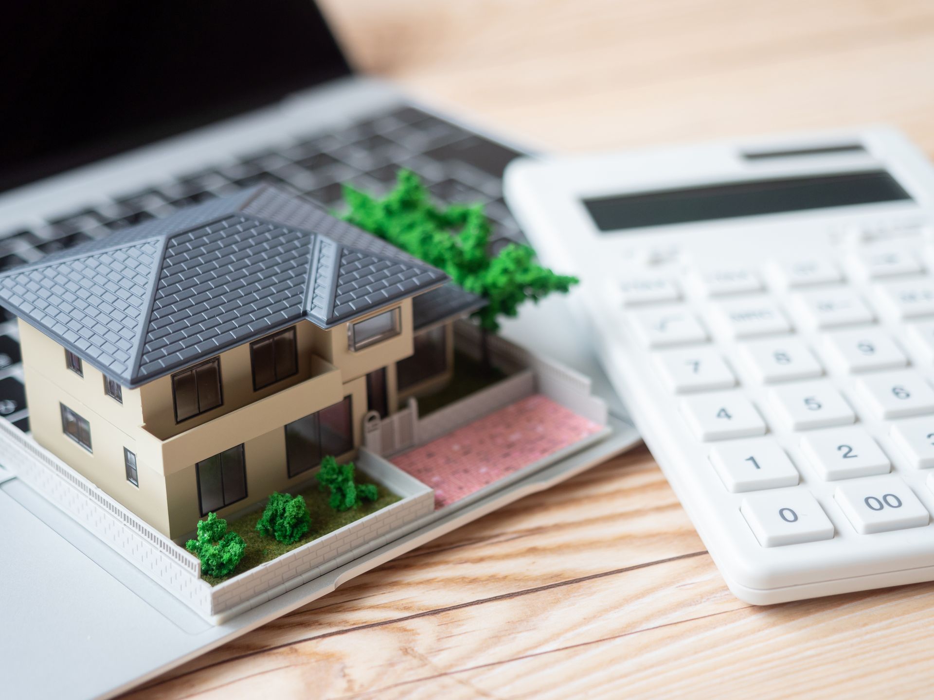 Maison miniature sur un ordinateur portable à côté d'une calculatrice.