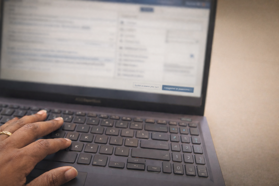 Main d'une personne tapant sur un clavier d'ordinateur portable ; l'écran est légèrement flou et affiche une interface web.