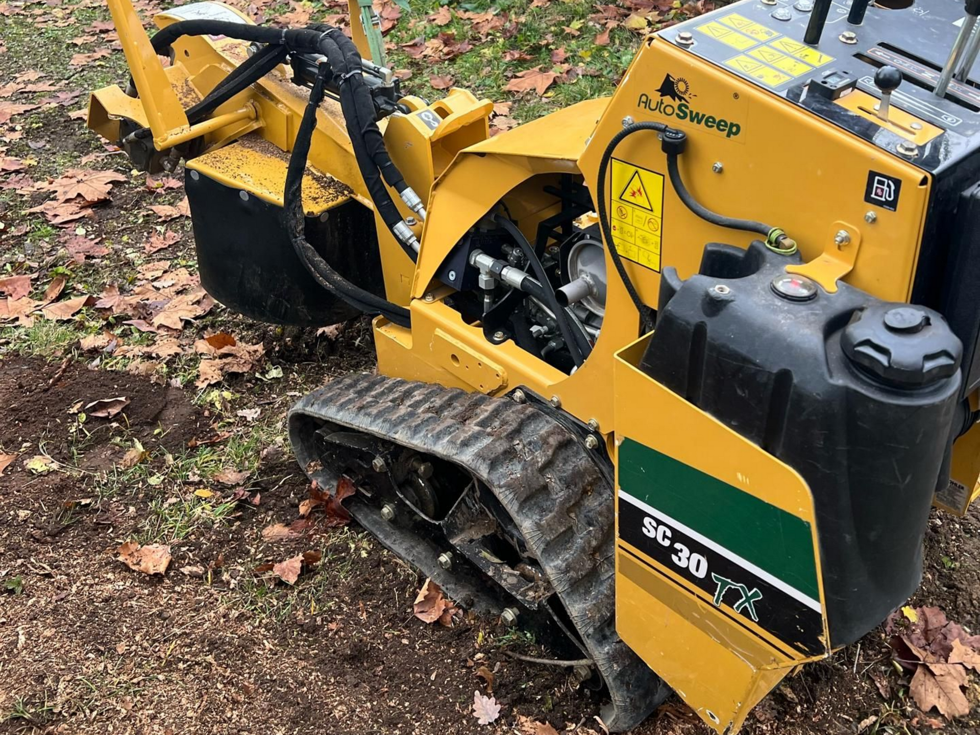 Engin utilitaire jaune à chenilles sur un sol recouvert de feuilles dans une zone boisée pour retirer une souche