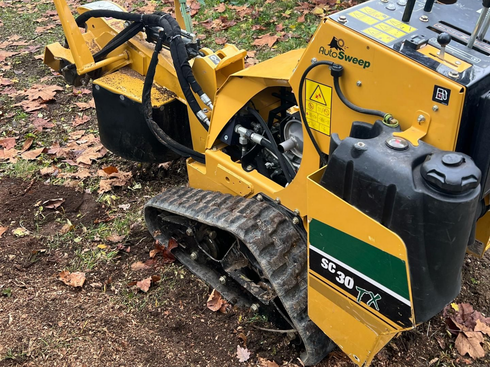Chargeuse compacte à chenilles jaune avec un godet noir qui retire des racines d'arbres