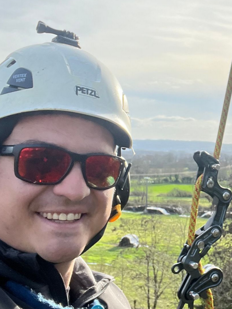 Élagueur portant un casque blanc et des lunettes de soleil dans un arbre.