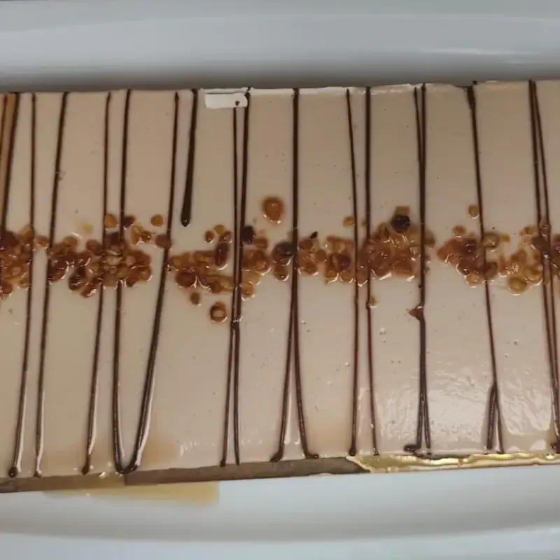 Postre rectangular con glaseado tostado, llovizna de chocolate y nueces picadas.
