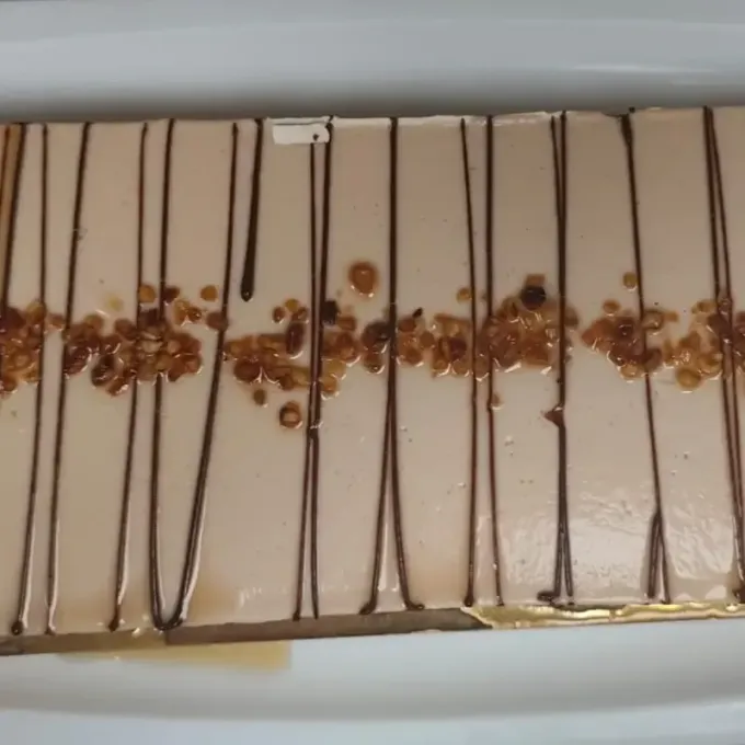 Postre rectangular con glaseado tostado, llovizna de chocolate y nueces picadas.