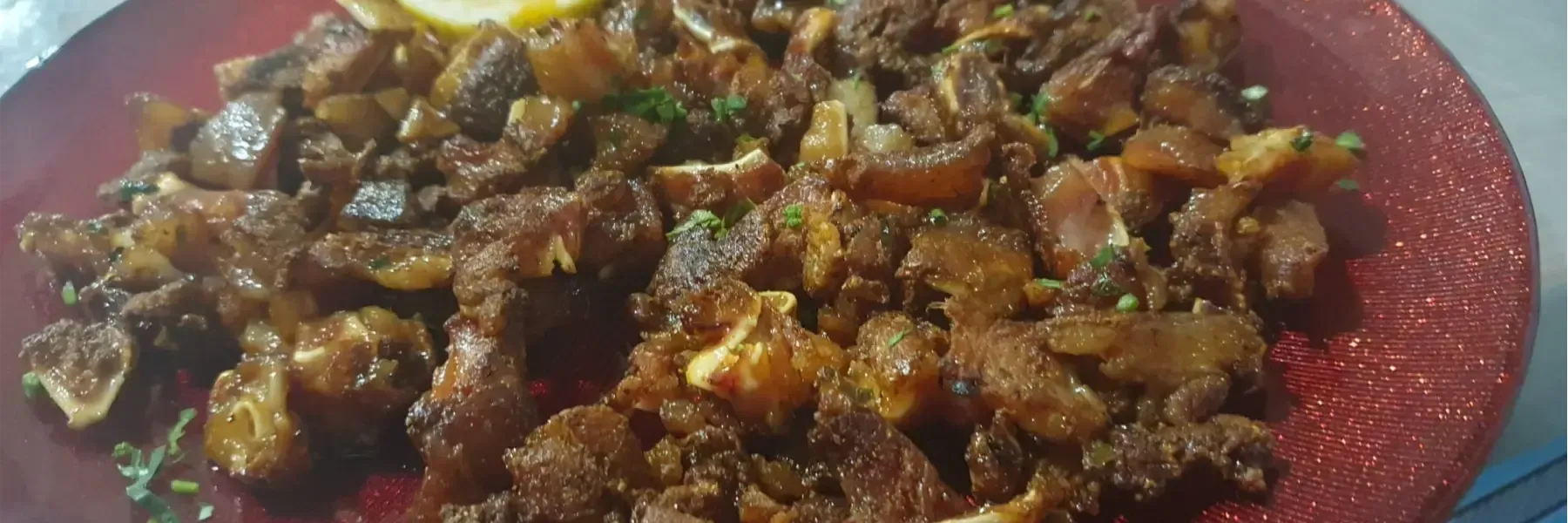 Comida cocinada de color marrón en un plato rojo. Rodajas de limón en la parte superior.