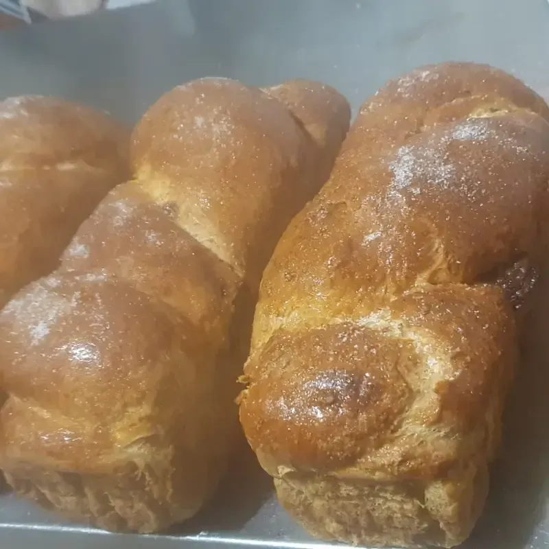 Panes dorados y trenzados espolvoreados con azúcar, expuestos en una bandeja.