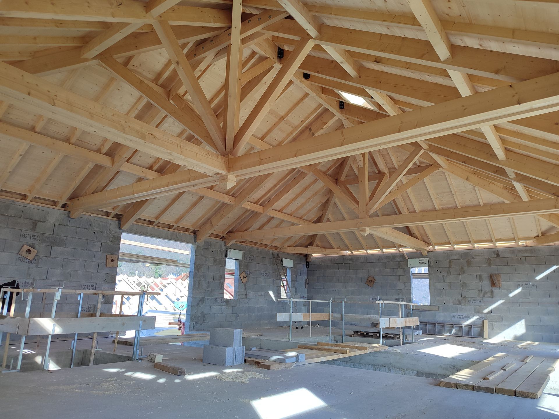 Vue intérieure d'un bâtiment en construction, montrant la charpente du toit en bois sur des murs en pierre grise.