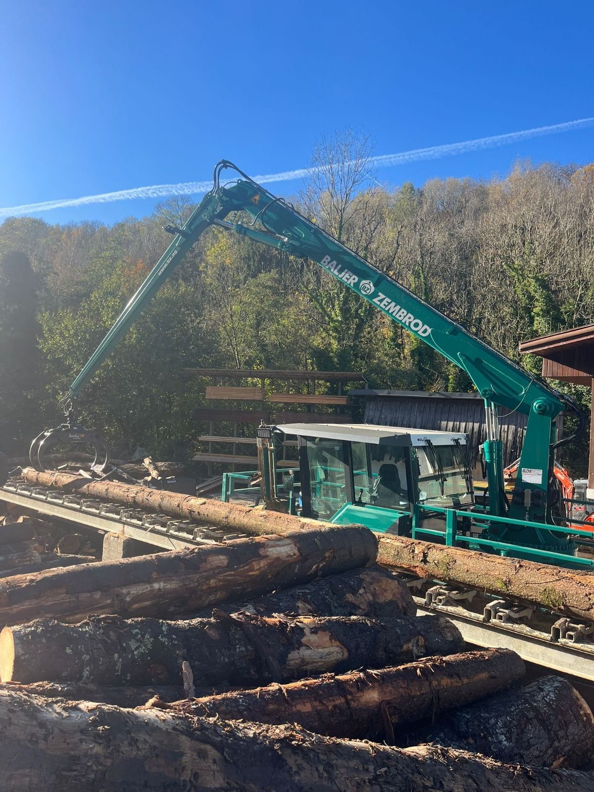 Une grume est traitée sur des machines de scierie industrielle ; de la sciure de bois est visible.
