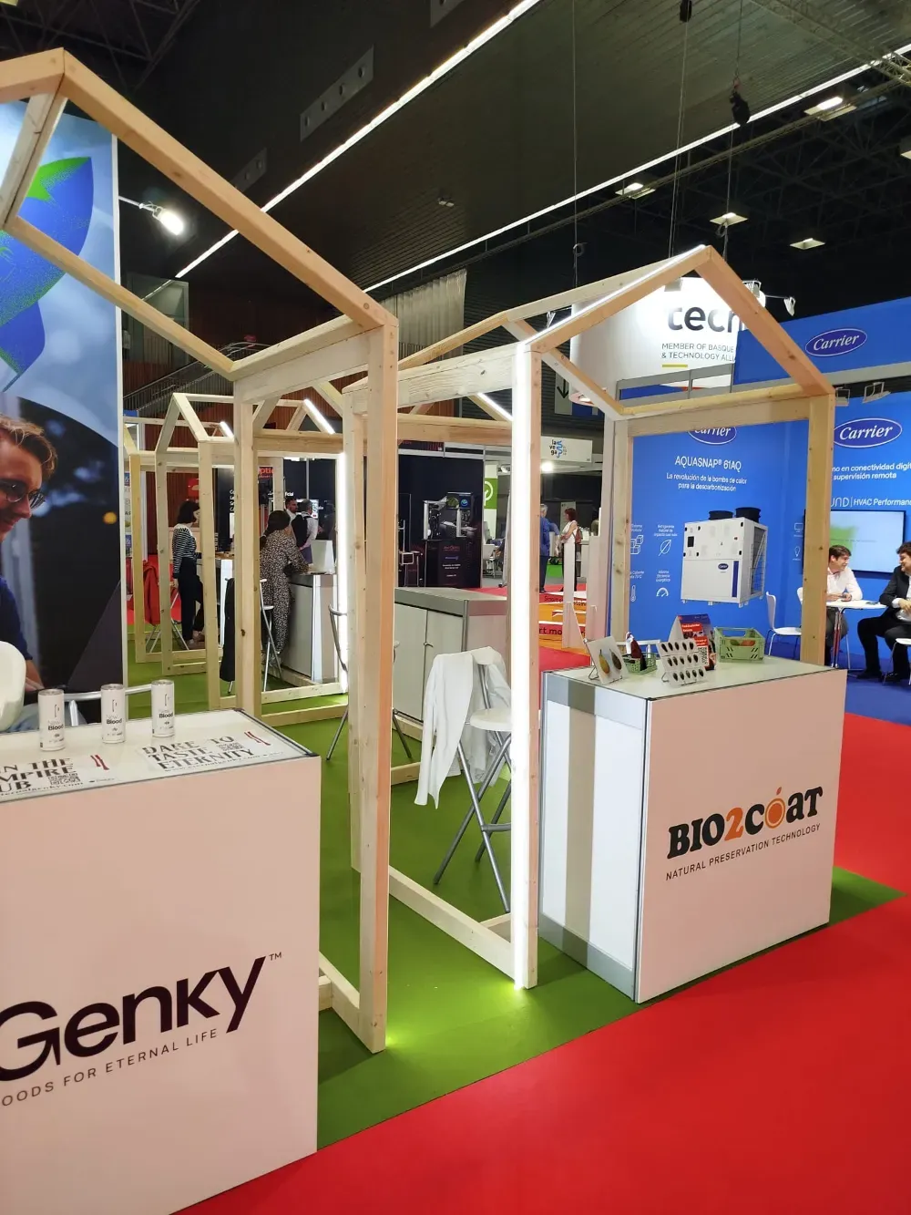 Stand de feria con estructura de madera blanca, moqueta verde y la marca Genky y BIOCARE.