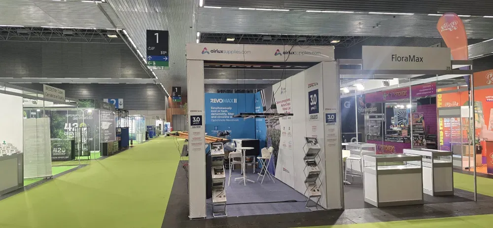 Stands de feria con suelo verde, expositores blancos y un pasillo central en un pabellón de exposiciones.