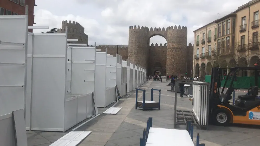 Escena callejera con barreras de construcción blancas, una puerta de piedra al frente y edificios a lo largo de la carretera.