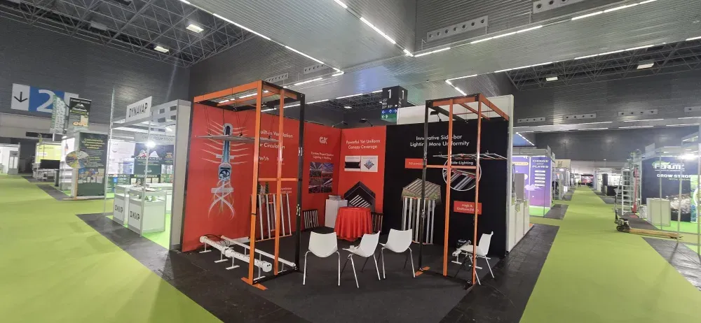 Stand de feria comercial con paneles de exhibición rojos, camisas colgadas y sillas blancas sobre un piso alfombrado de negro.