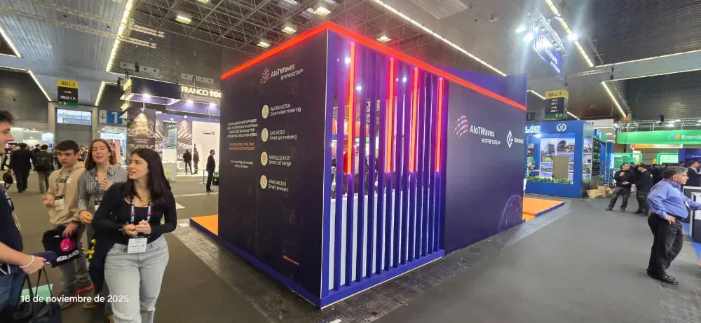 Stand de feria con luces verticales brillantes, gente cerca y una gran pantalla en un salón de convenciones.