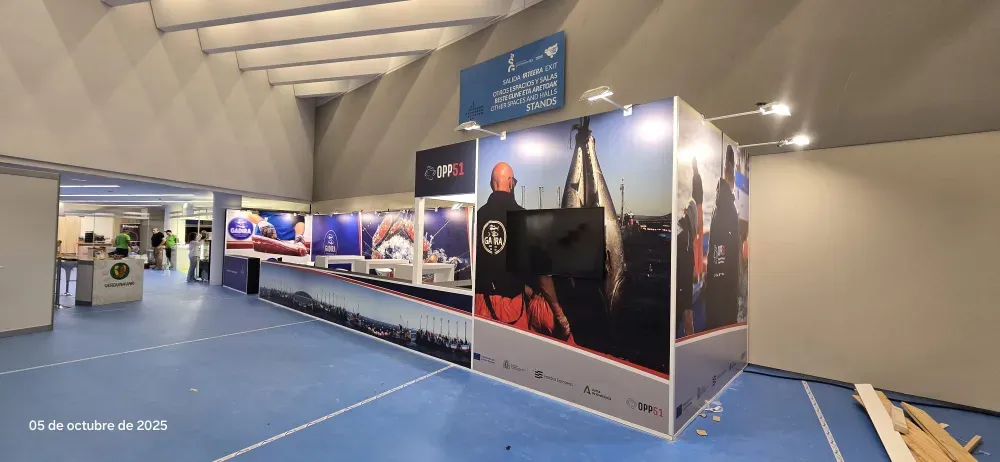 Stand de exposición interior con moqueta azul, grandes paneles fotográficos y un pasillo con techo curvo.