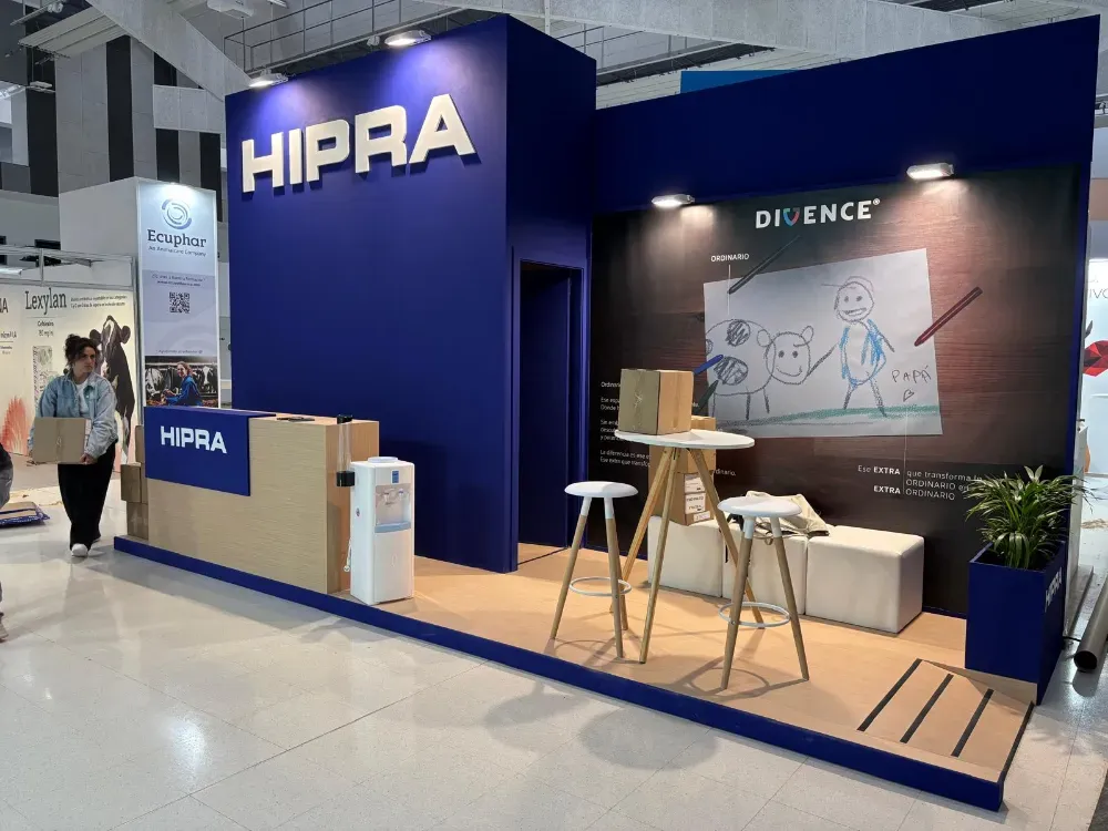 Stand de HIPRA en la feria comercial con paredes azules, una zona de descanso, taburetes y un telón de fondo con la marca.