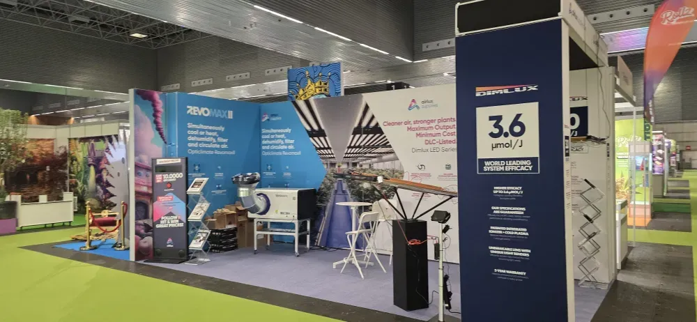 Stand de feria comercial con exhibidores azules y verdes, pancarta alta con el número "3.6" y área de asientos en un salón de convenciones.