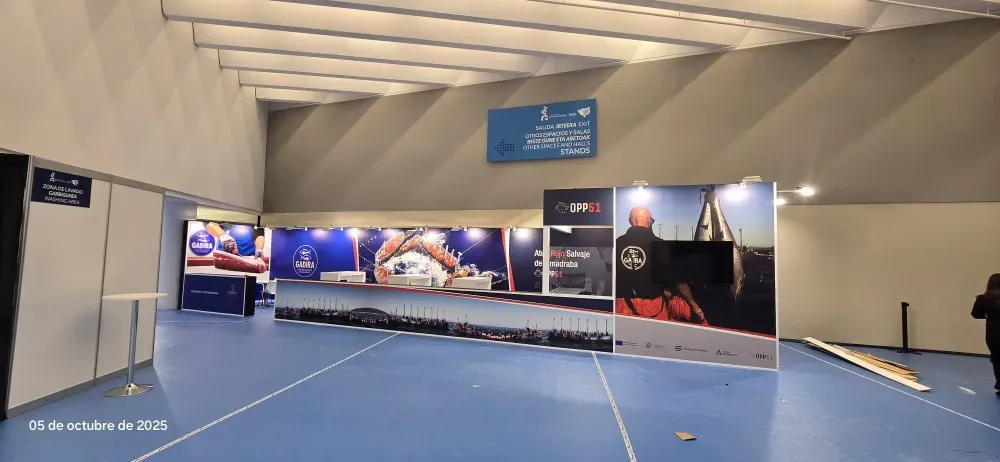 Pabellón deportivo cubierto con colchonetas azules y grandes pancartas publicitarias a lo largo de la pared.