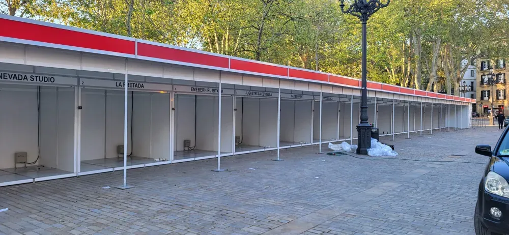 Estructura de estacionamiento exterior vacía con bahías blancas, detalles de techo rojos y árboles al fondo.