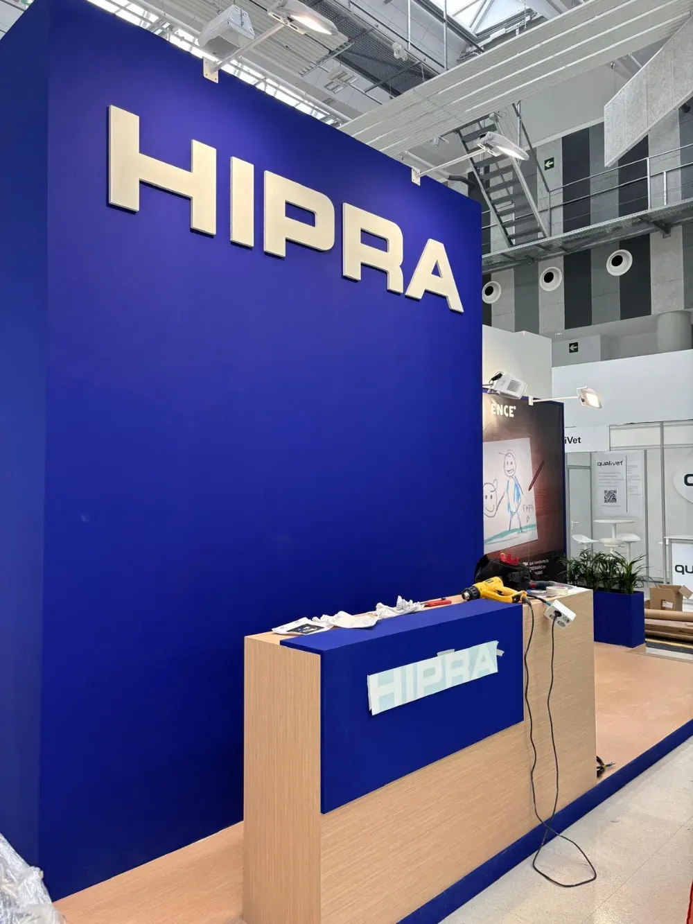 Stand de HIPRA en la feria, con una gran pared azul y mostrador de recepción de madera.