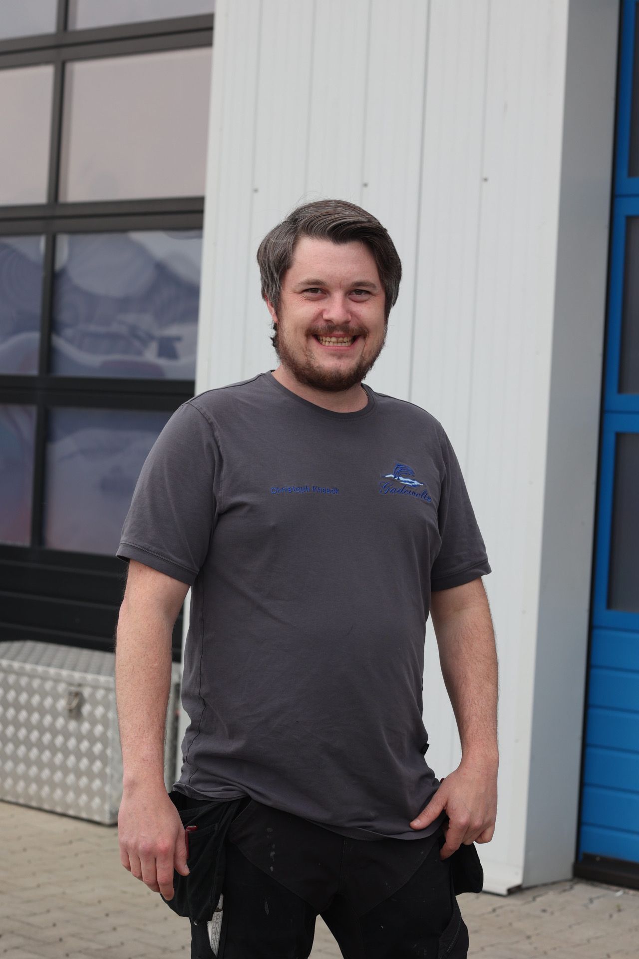 Ein Mann mit Bart steht vor einem Gebäude.