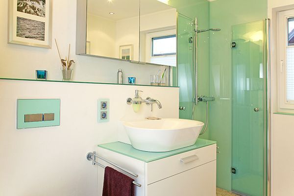 Modernes Badezimmer mit weißem Waschbecken, mintgrüner Dusche und weißem Schrank.