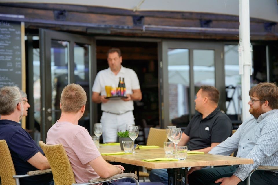 Ein Kellner serviert einer Gruppe von Männern, die an einem Restauranttisch im Freien sitzen, Getränke.