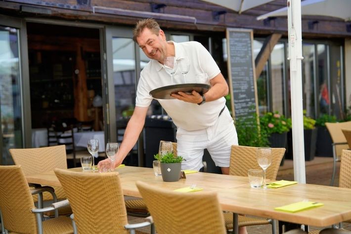 Kellner deckt draußen in einem Restaurant einen Tisch und hält ein Tablett.