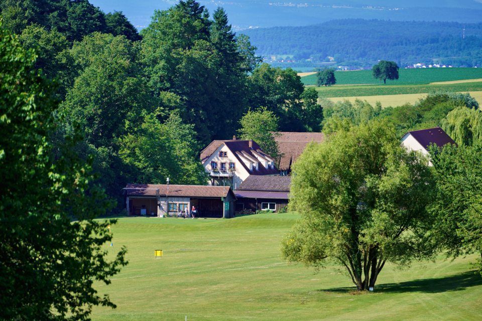 Auf einer grünen Wiese steht ein Haus, umgeben von Bäumen mit einer gelben Flagge.