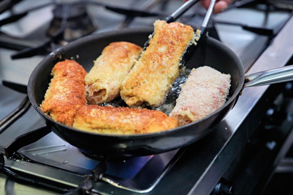 Person brät panierte Brötchen in einer Pfanne auf einem Herd.