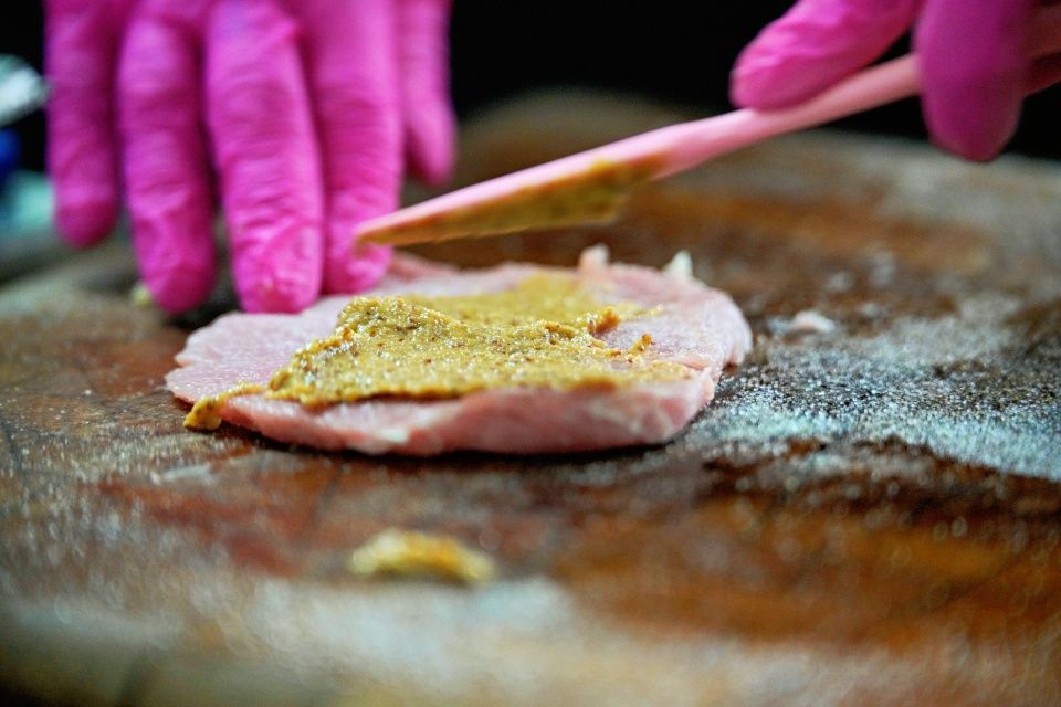 Hände in rosa Handschuhen verteilen Senf auf Fleisch.