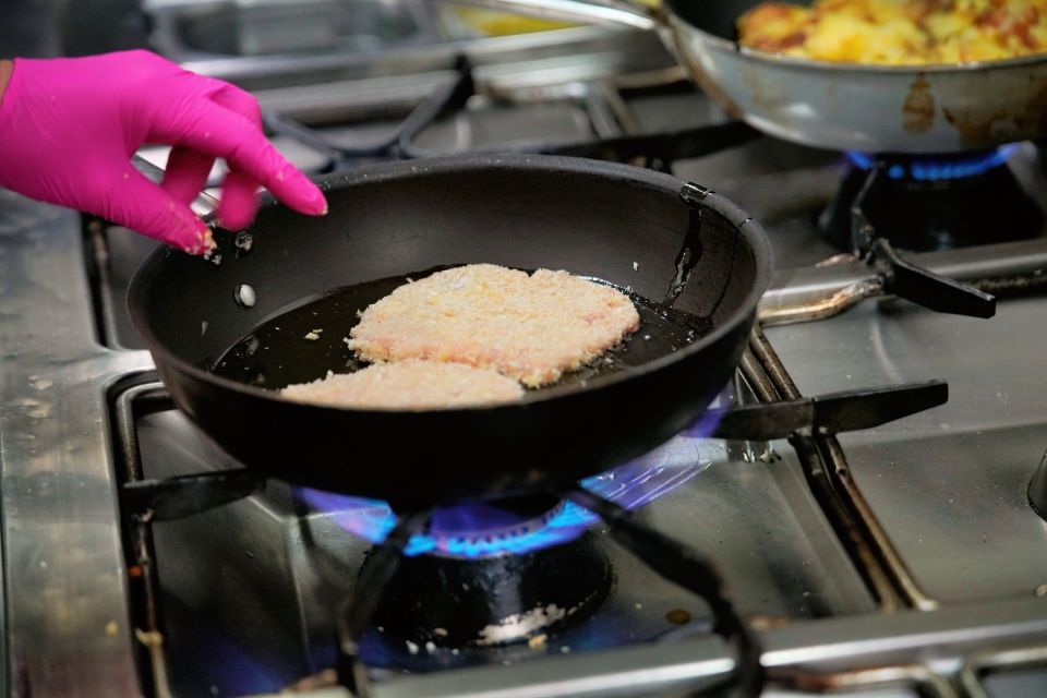 Person mit rosa Handschuhen brät panierte Schnitzel in einer Pfanne auf einem Gasherd.